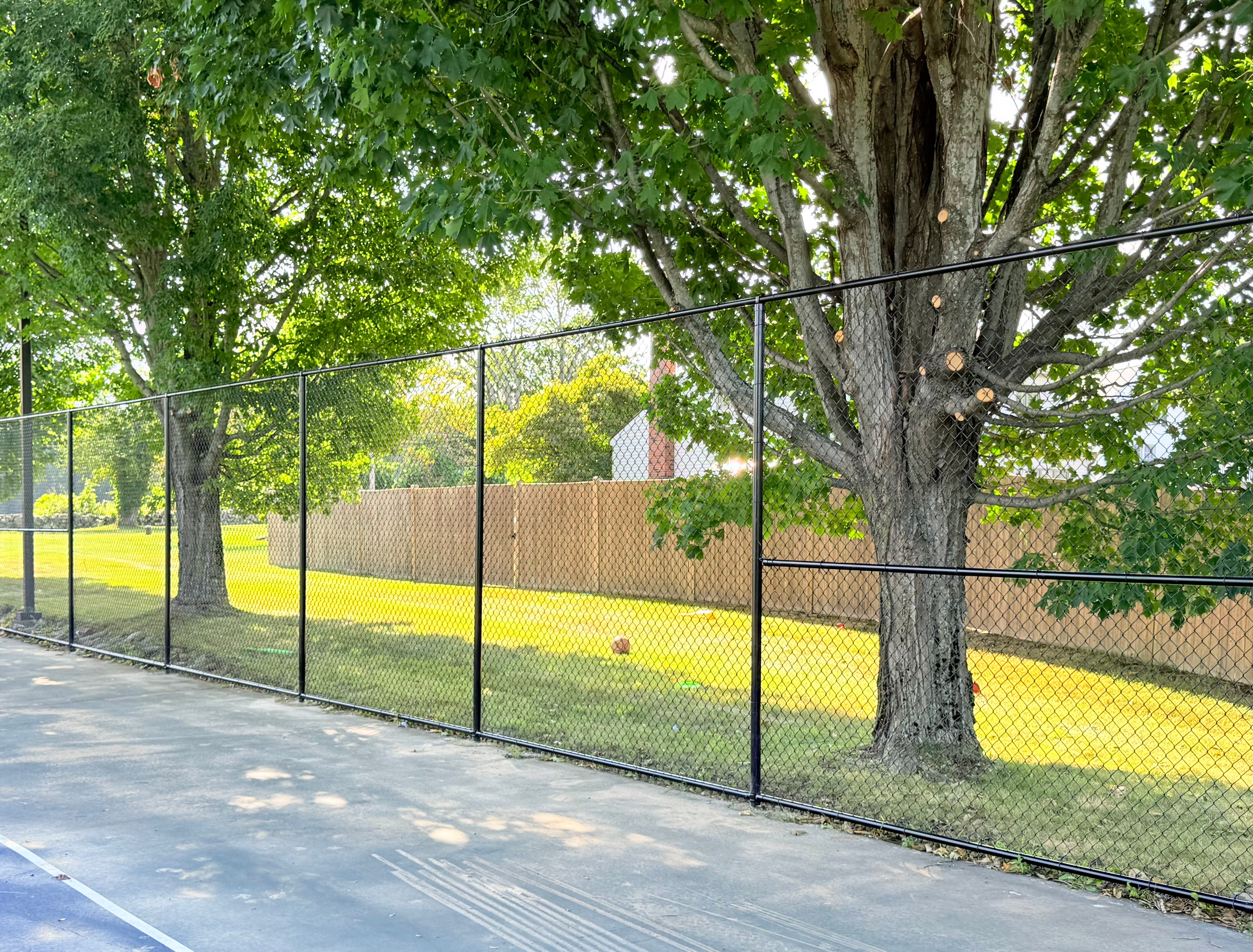 Black chain link fence enclosing large outdoor area in autumn by Ultra Fence LLC